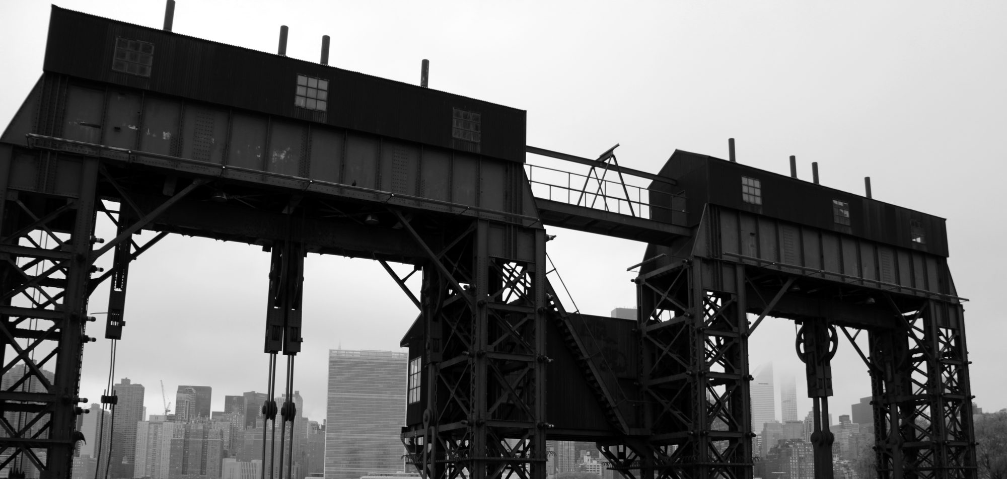 Two steel gantries joined by a walkway, with the Manhattan skyline visible between their legs